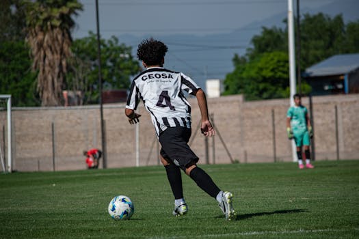 Young soccer player dribbles ball on outdoor field during match.