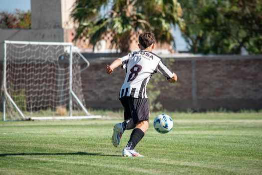 A soccer player in action, wearing a striped jersey, kicking a ball towards the goal during a sunny day match.