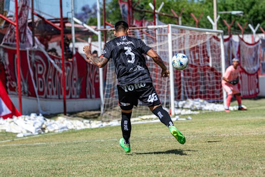 A soccer player in action kicking a ball during a match on a sunny day.