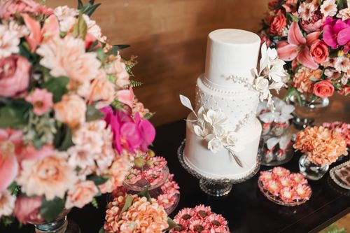 Free A white wedding cake surrounded by vibrant pink and orange floral arrangements, creating a luxurious setting. Stock Photo