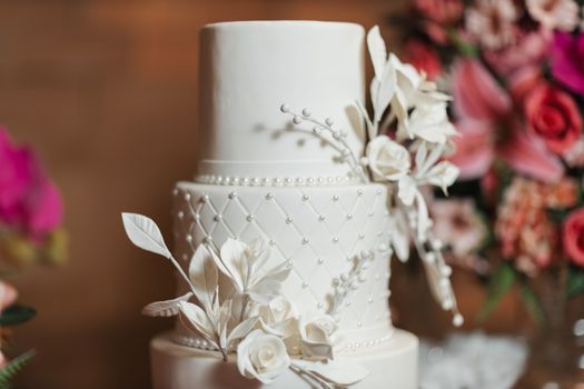 A beautifully detailed three-tier white wedding cake adorned with delicate white flowers and pearls.
