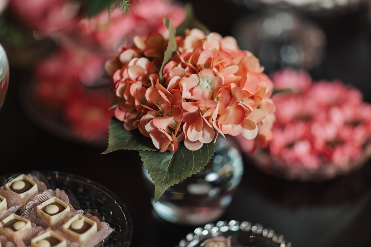 A close-up of pink hydrangeas in a vase surrounded by elegant confections on a dark table.