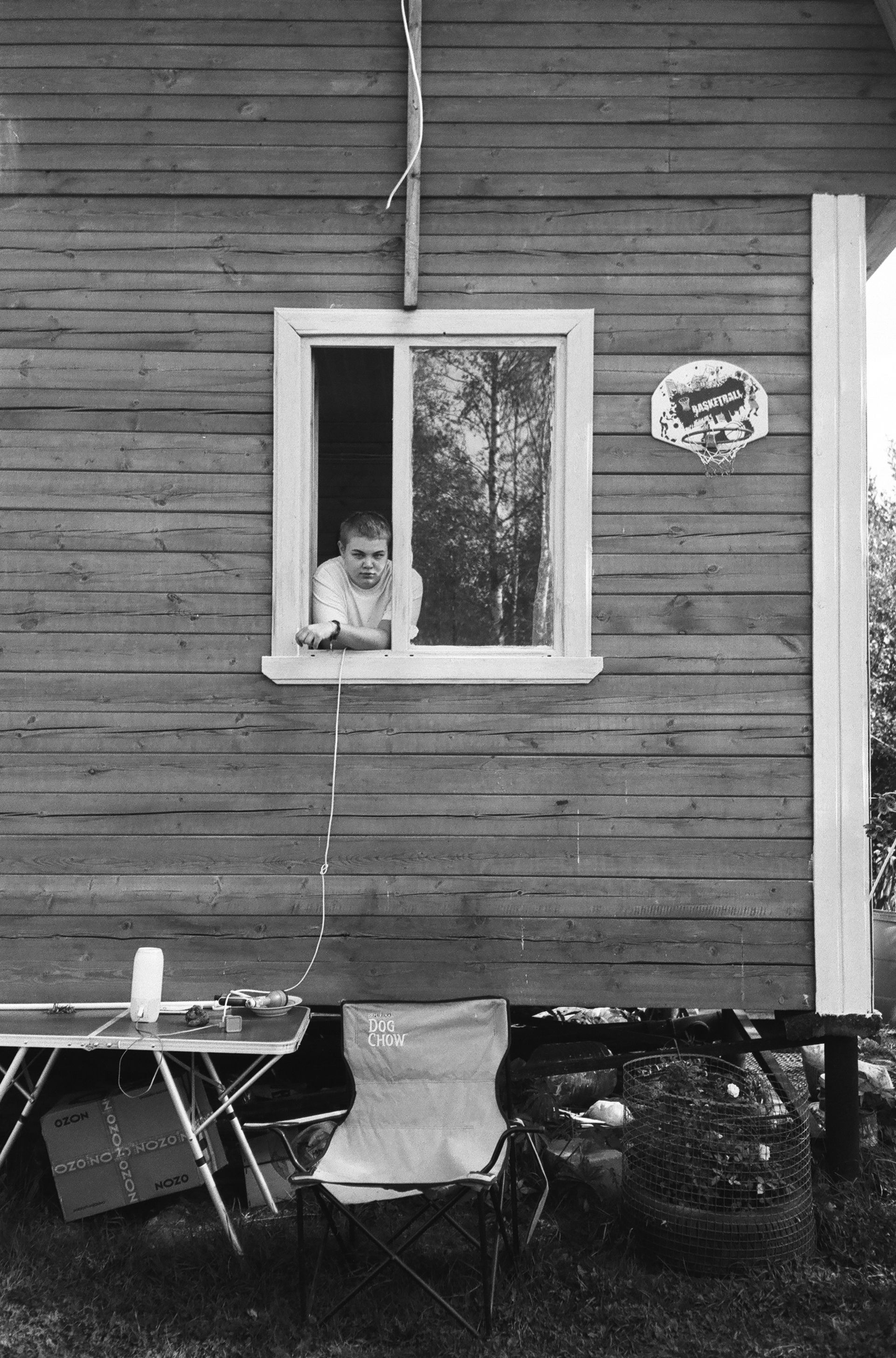 A man looks out a wooden cabin window, captured in black and white photography.