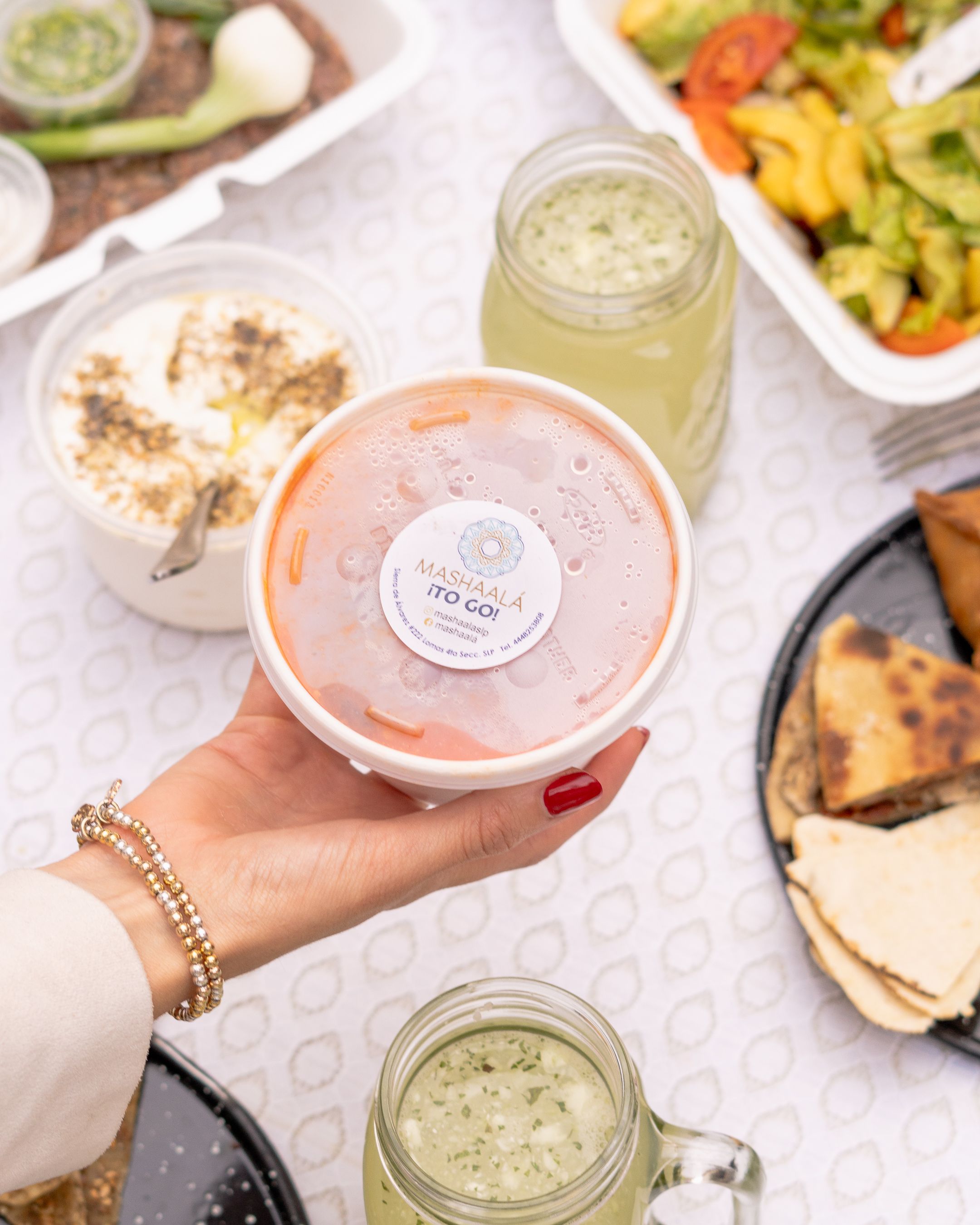 Hand holding Lebanese food container amidst an assortment of dishes, showcasing a vibrant meal setting.