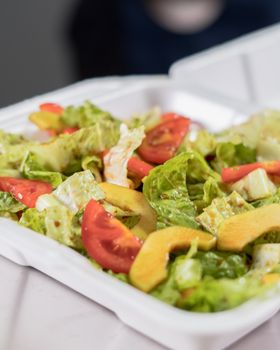 A vibrant mixed salad with tomatoes, lettuce, and cucumber in a takeaway box.