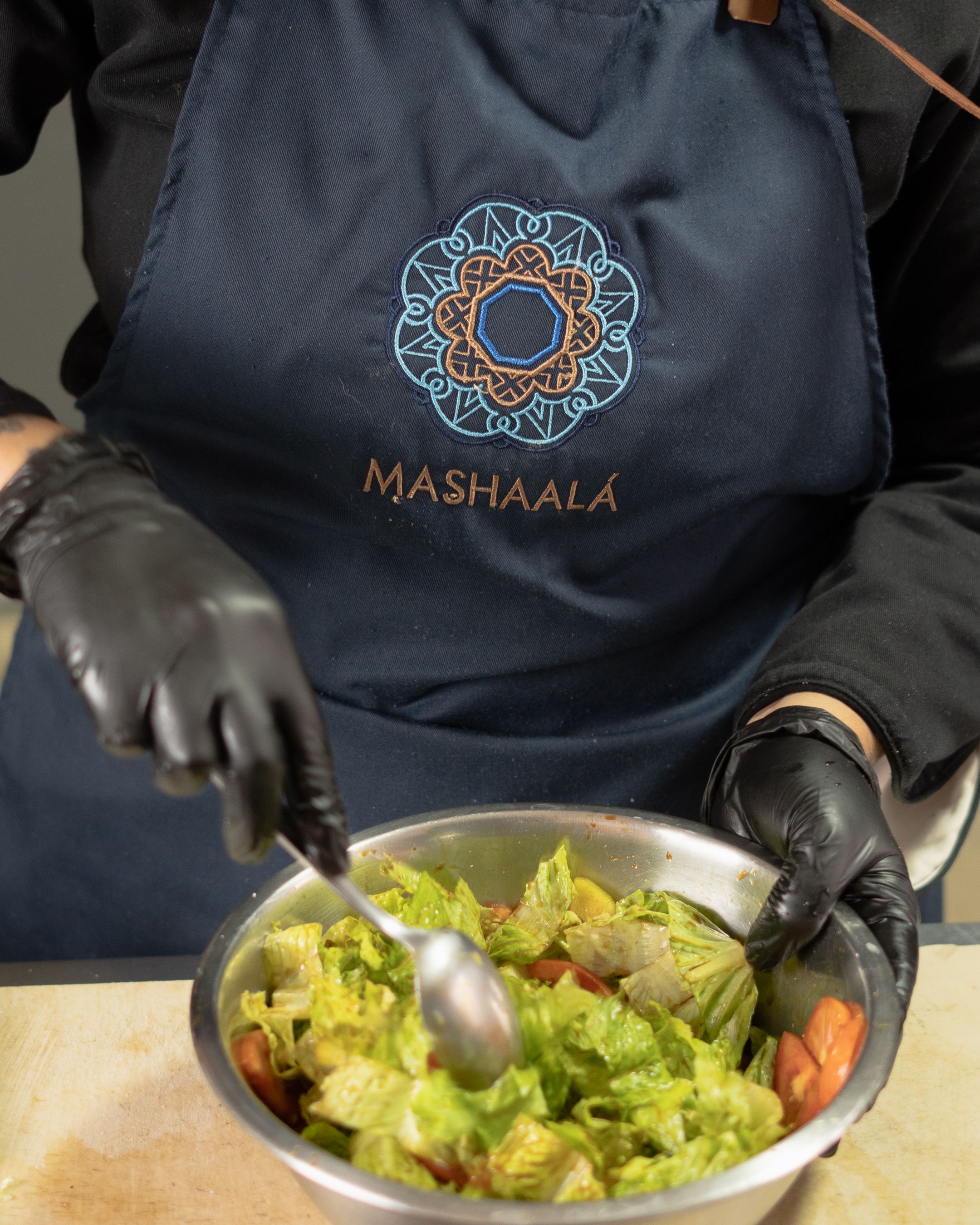 A chef in Santiago de Querétaro mixes a fresh salad, wearing a Mashaalá apron and gloves.