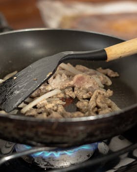 Close-up of meat and onions sizzling in a skillet over a gas stove.