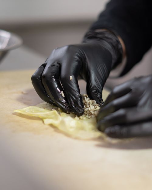 Free Hands wearing gloves skillfully prepare cabbage rolls in a kitchen setting. Stock Photo