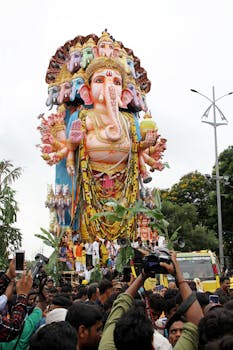 Colorful Ganesh Chaturthi procession with giant Ganesha statue in Hyderabad, India, amidst a lively crowd.