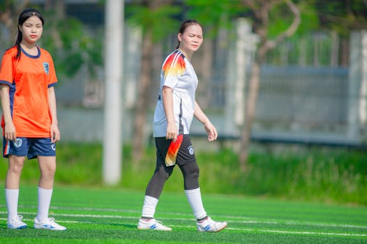 Two East Asian female soccer players on a bright day at a field in Hanoi, Vietnam.