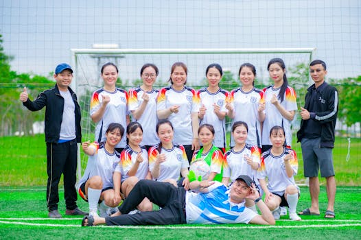 Women's soccer team and coaches pose cheerfully on a football field in Hanoi, Vietnam.