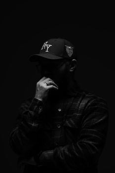 Black and white portrait of a mysterious figure in a low-key setting wearing a cap and plaid shirt.
