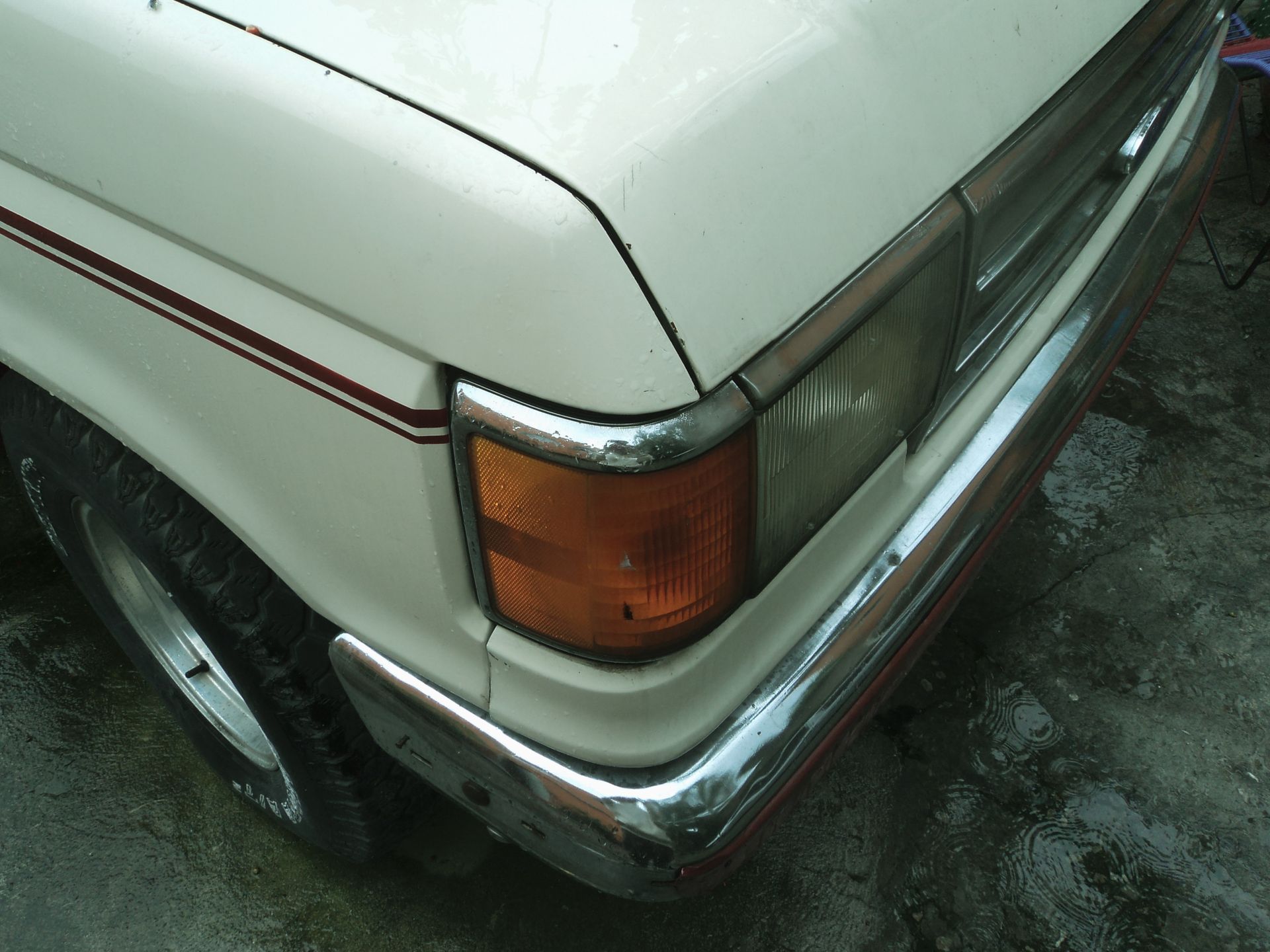 Detailed shot of a vintage car's front end with focus on the headlight and grill.