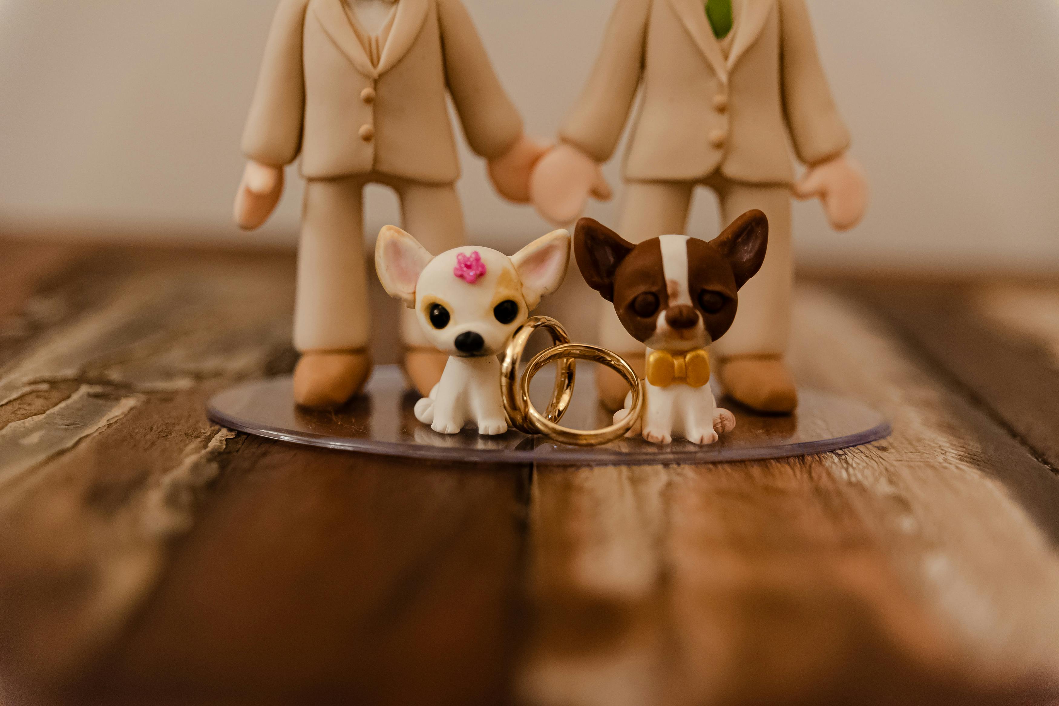 A charming wedding cake topper featuring two dogs with wedding rings, set against a wooden background.