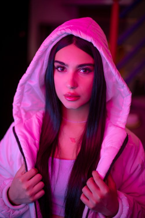 Free A striking portrait of a woman in a neon pink hoodie with vibrant lighting. Stock Photo