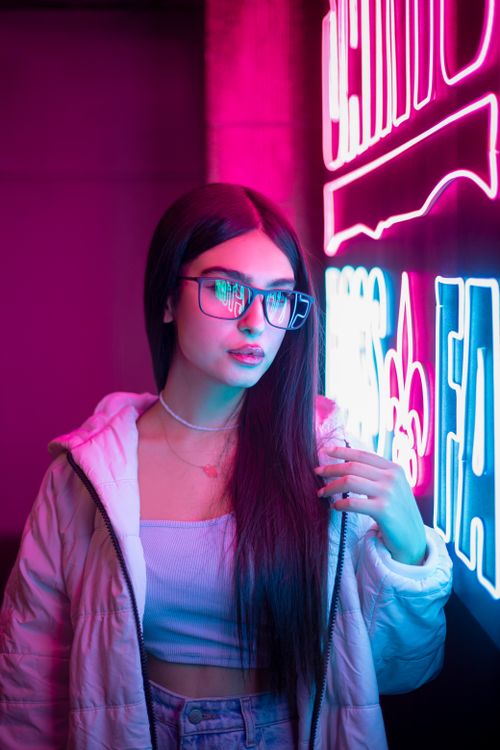 Free Fashionable woman in glasses poses next to vibrant neon lights, creating an urban nightlife vibe. Stock Photo