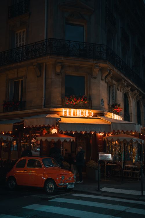 Free Cozy Parisian restaurant ambiance with a vintage Fiat 500 at night in Paris, France. Stock Photo