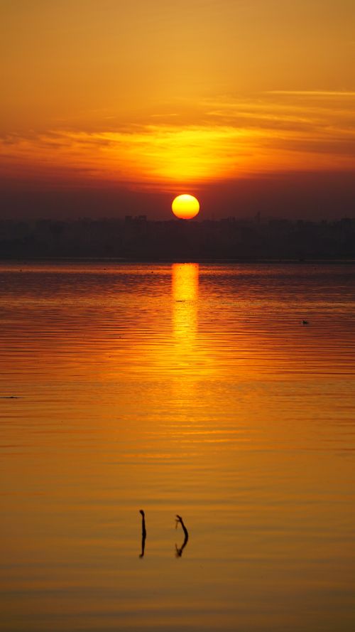 Free Beautiful sunrise over a calm lake with vibrant orange hues and sun rays in Hyderabad, India. Stock Photo