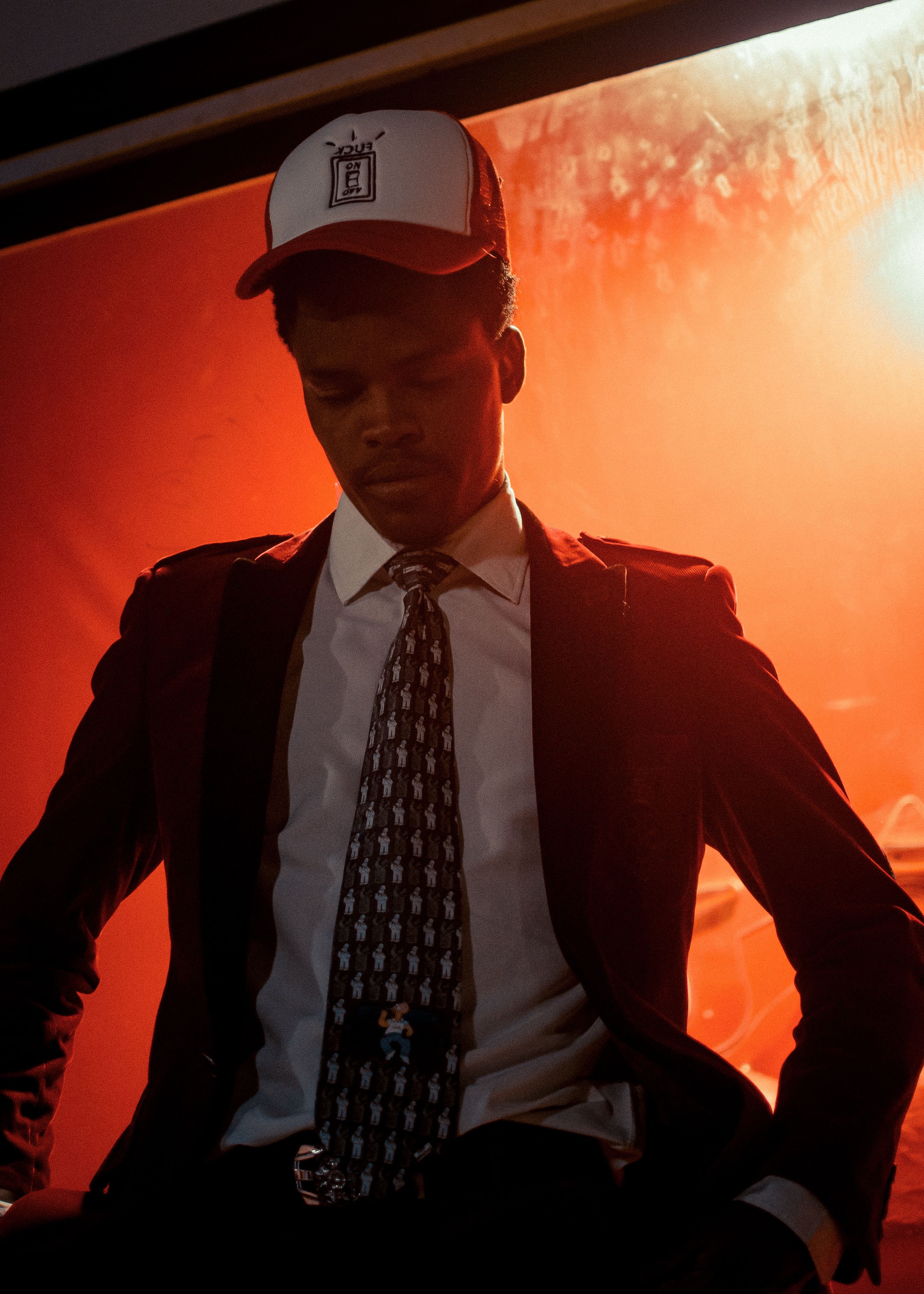 Man in formal outfit and cap, sitting in dramatic lighting. Stylish and contemplative.