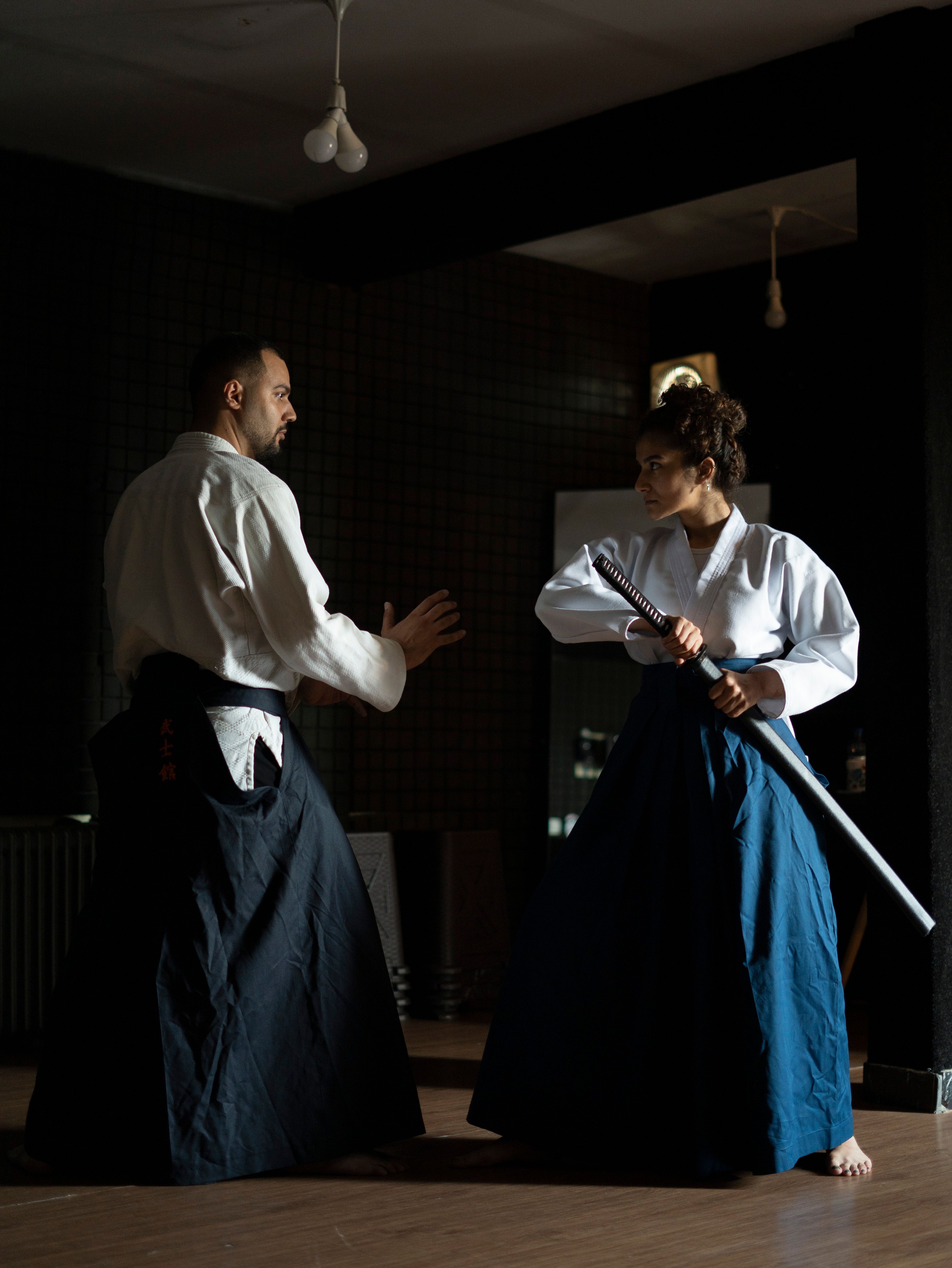 Two individuals practicing martial arts with swords in a dimly lit room.