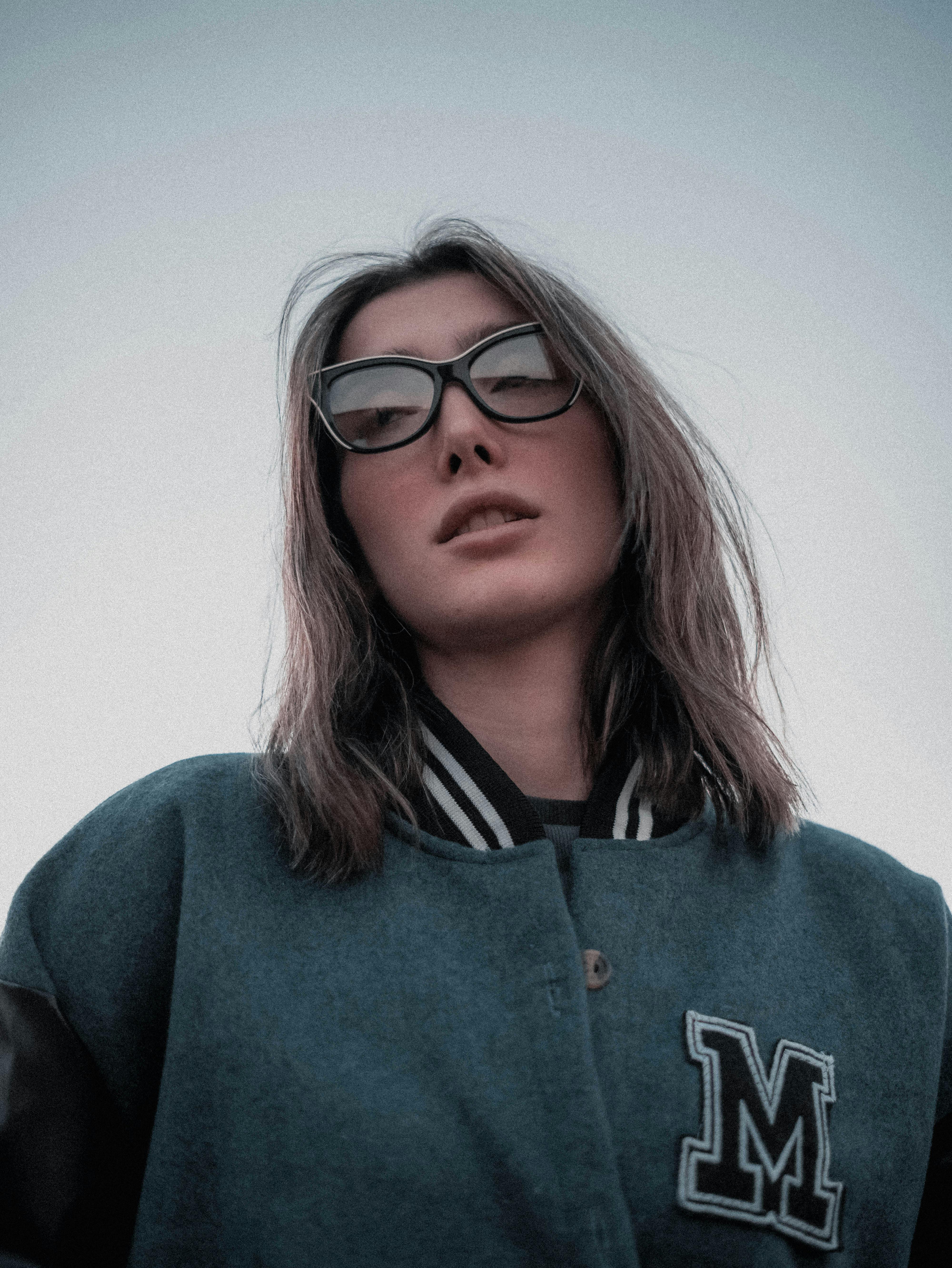 Portrait of a stylish young woman wearing glasses and a varsity jacket, exuding confidence.
