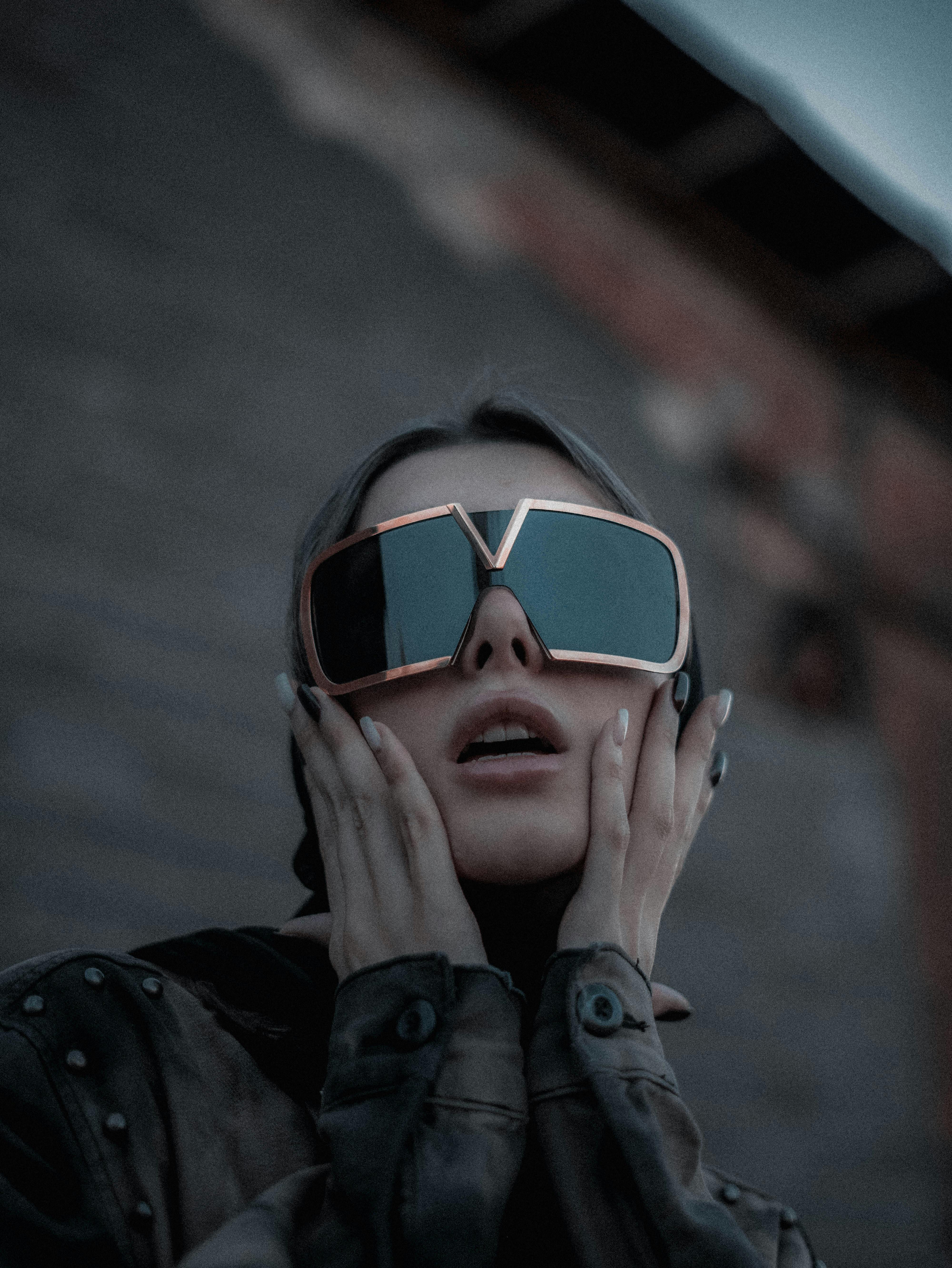 Model wearing oversized stylish sunglasses and futuristic attire, posing dramatically.