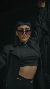 Fashionable woman wearing sunglasses and a black outfit in a stylish pose.