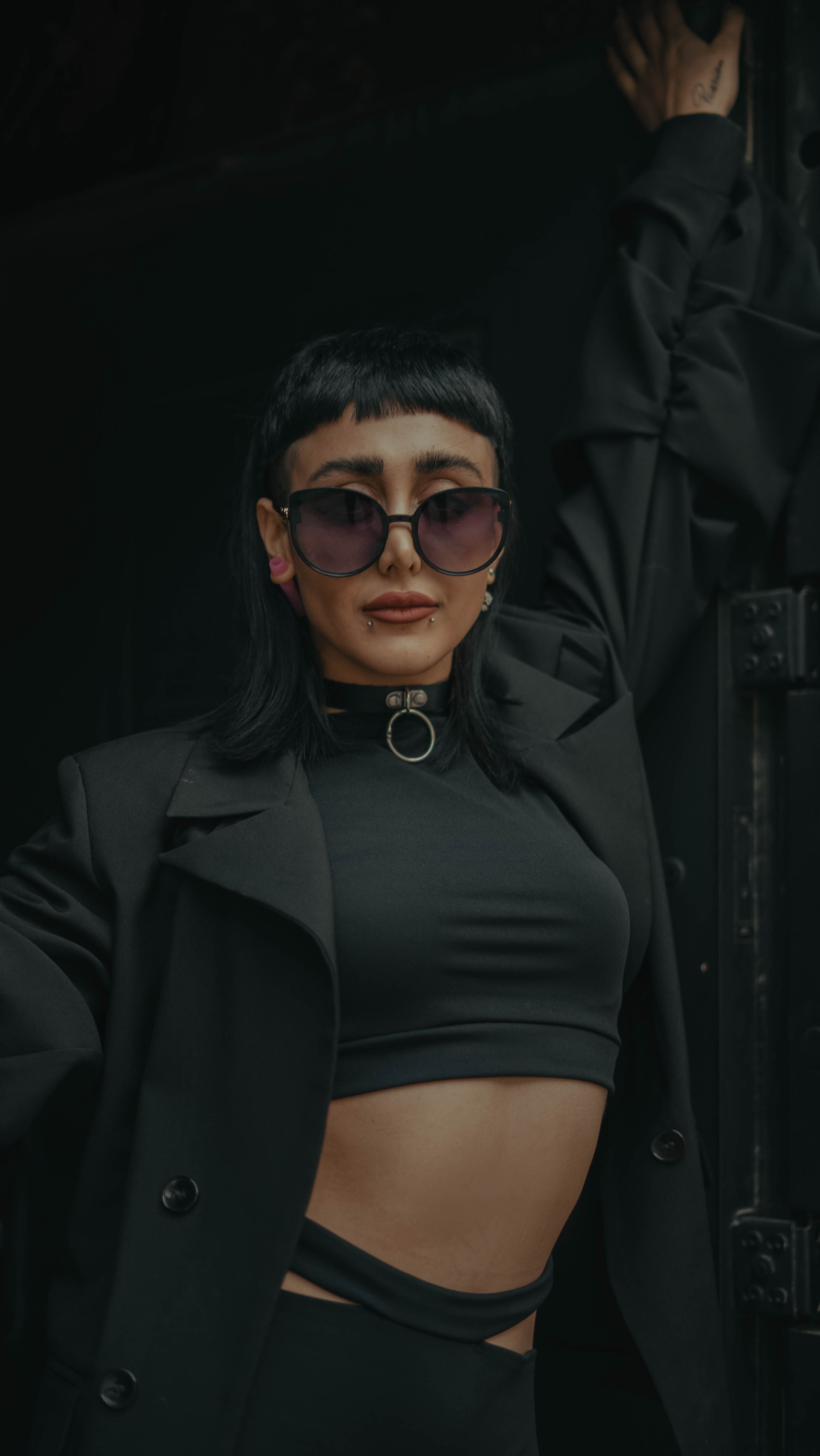 Mulher elegante usando óculos escuros e uma roupa preta em uma pose estilosa.