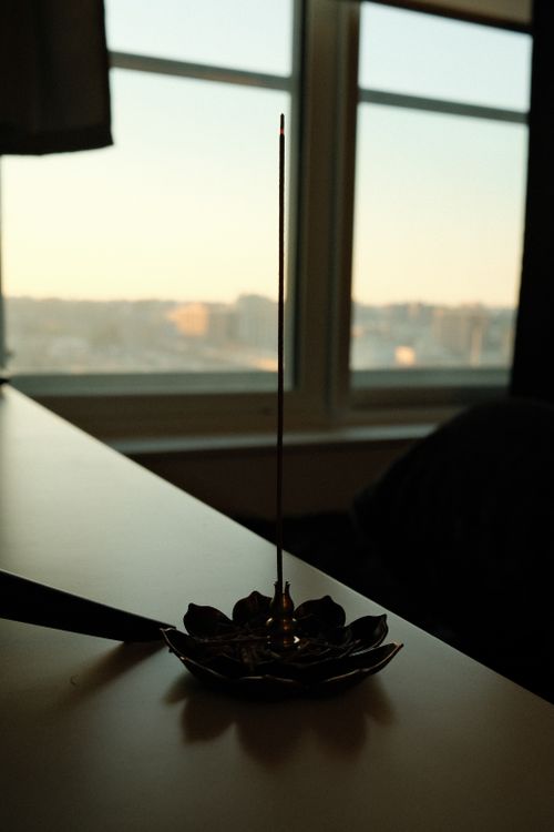 Free Incense burning in a decorative holder by a window during sunrise enhances relaxation mood. Stock Photo