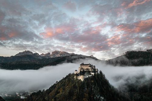 Free Majestic Hohenwerfen Castle surrounded by mist and mountains at dawn, Austria. Stock Photo