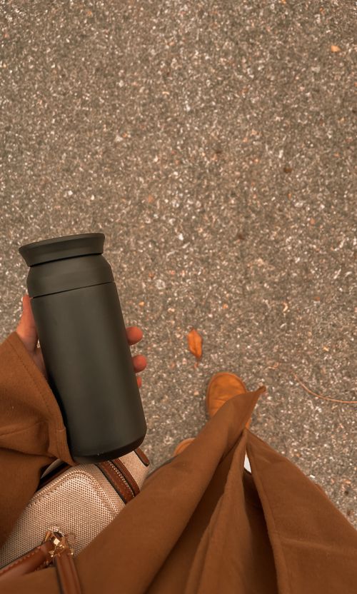 Free Person holding a black travel mug during an autumn walk on a textured path. Stock Photo