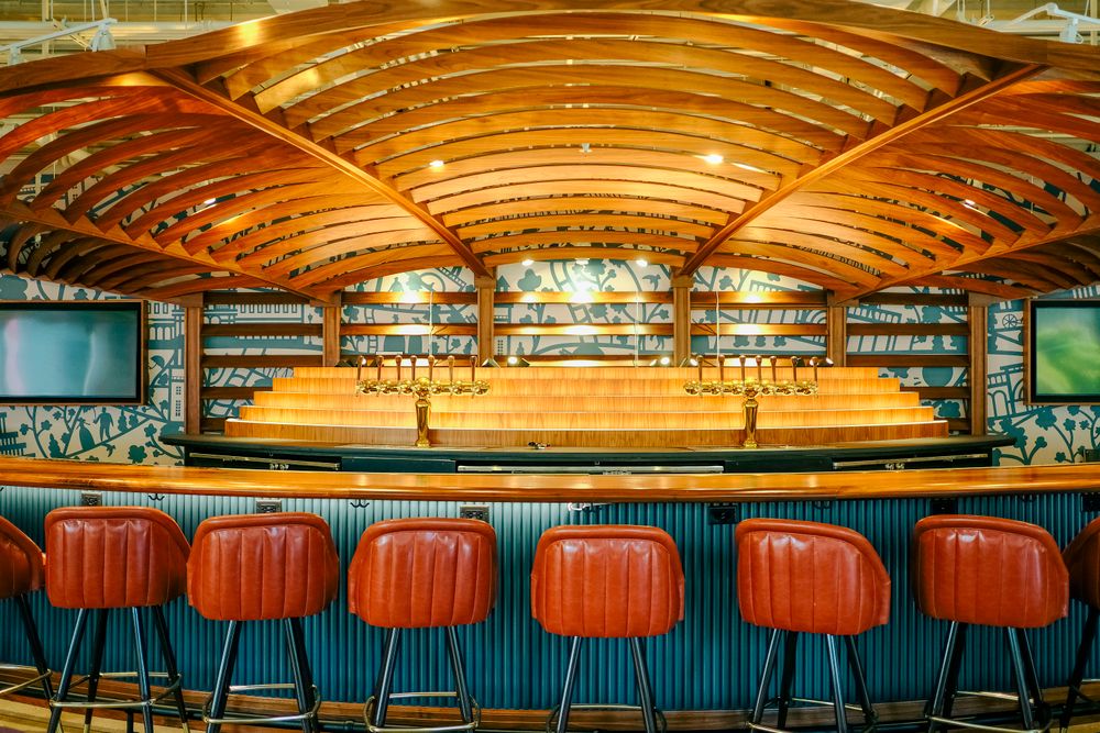 Bar elegant cu scaune înalte tapițate în piele portocalie, sub un tavan sculptat din lemn