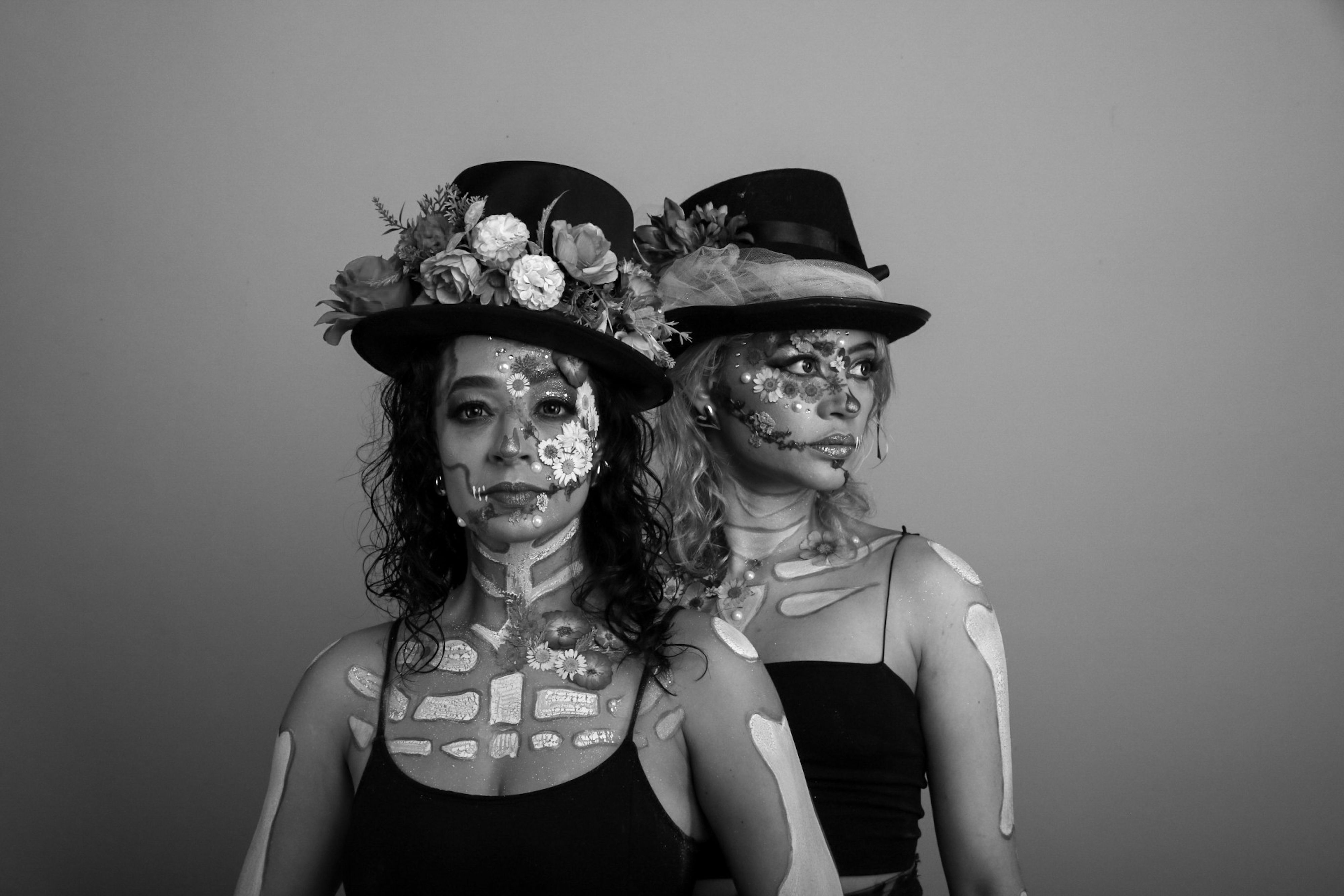Black and white portrait of two women with face paint and floral hats in artistic style.