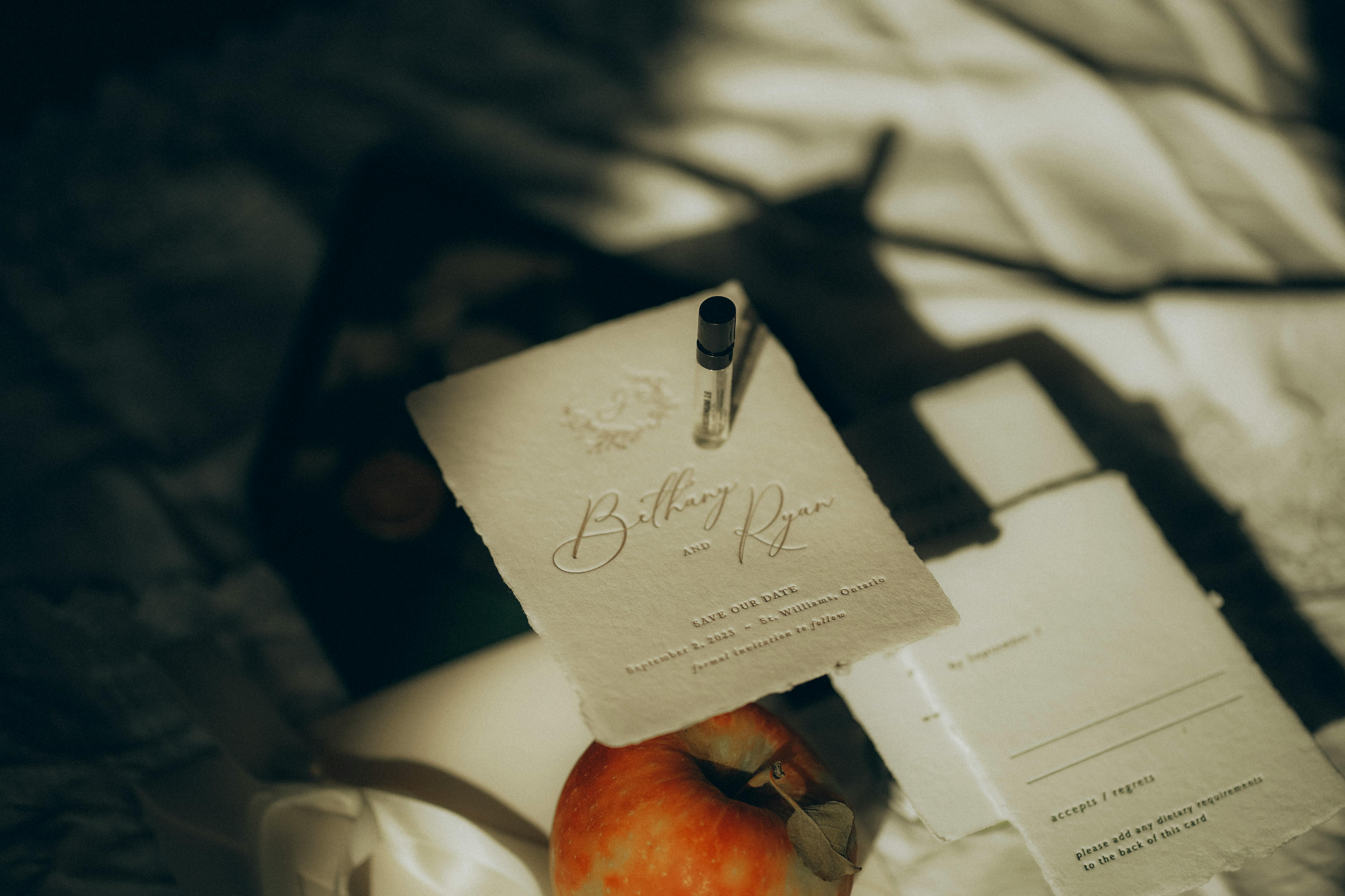 Kostenlos Künstlerisches Flatlay mit einer eleganten Save-the-Date-Karte mit sanften Schatten, einem Apfel und einem Parfümfläschchen. Stock-Foto