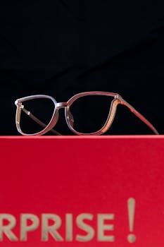 Close-up of fashionable eyeglasses against a bold red backdrop with surprise text.