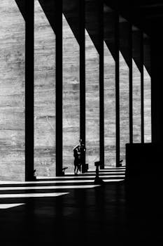 Black and white photo of dramatic shadows cast by architectural pillars, featuring two silhouettes.