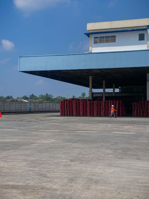 Warehouse exterior with stacked red pallets and workers under clear sky.