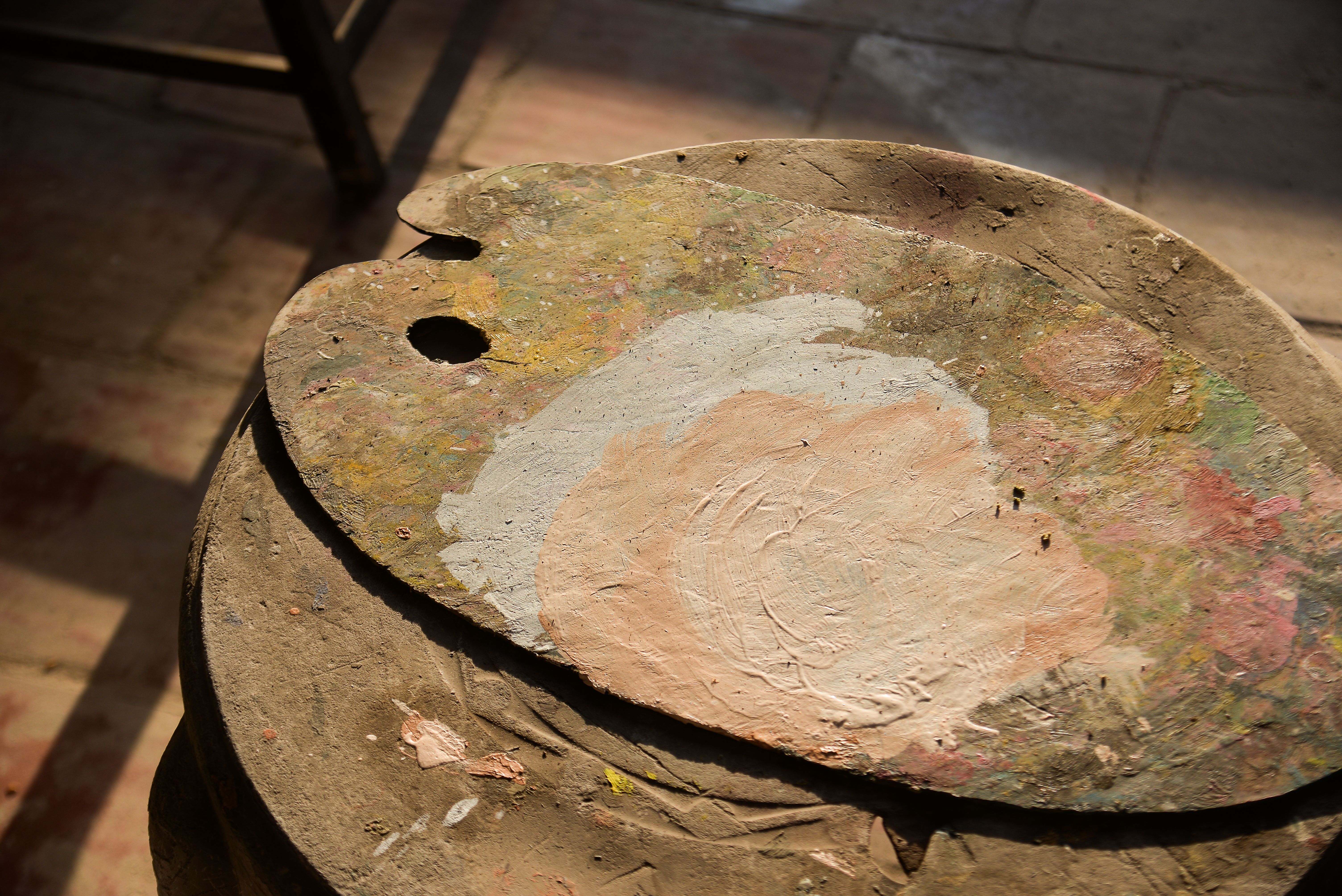 A sunlit rustic wooden painter's palette with mixed colors laid on a wooden surface.