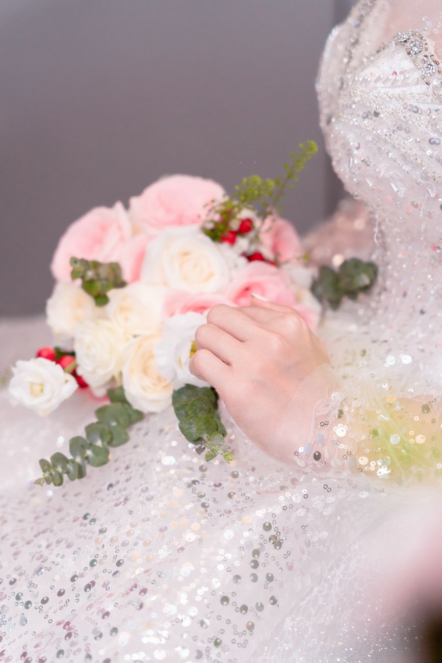 Close-up of a bridal gown with sequins and a bouquet of pink and white roses.
