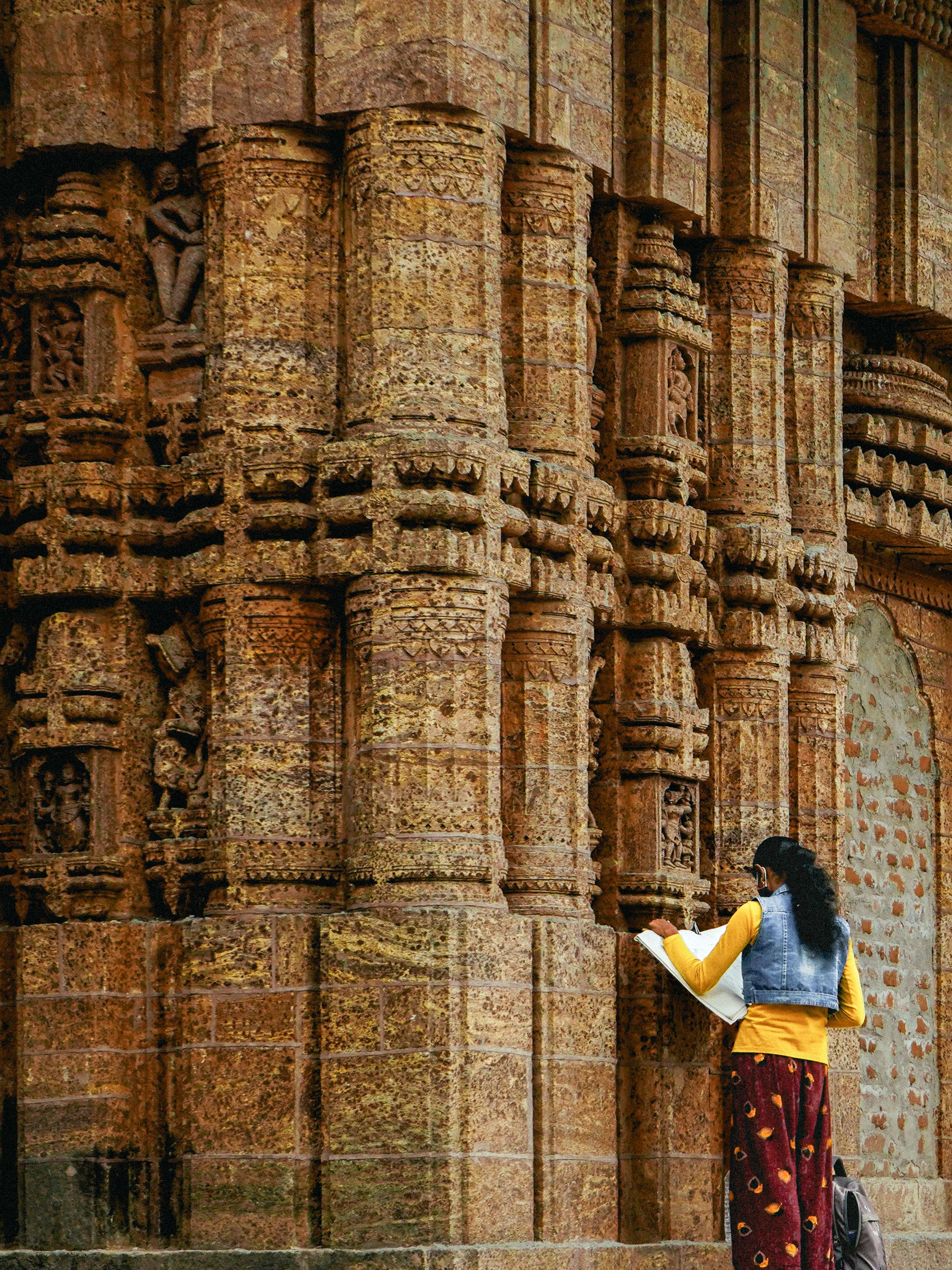 A woman explores intricate stone carvings on an ancient temple wall.