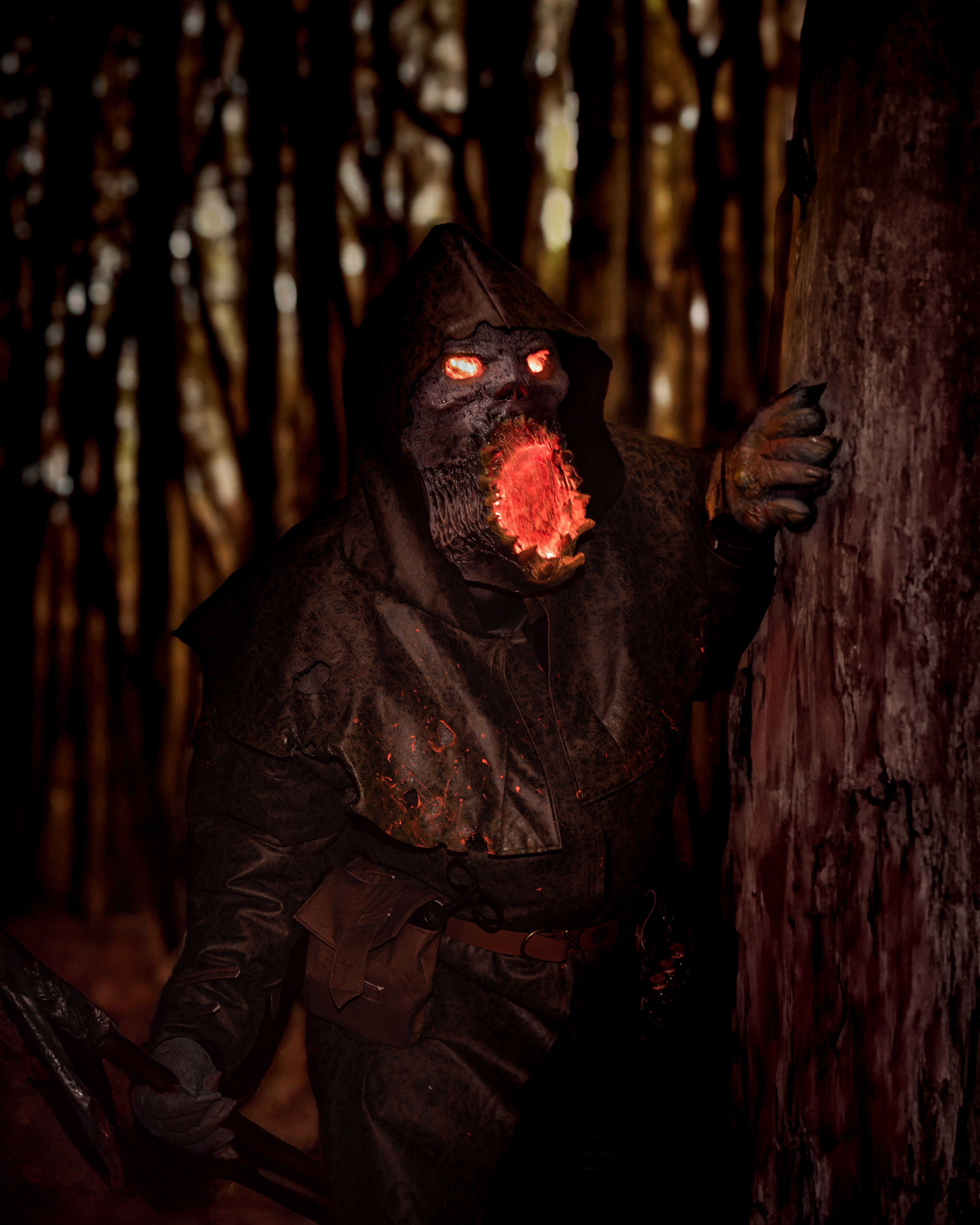 Horror-themed image of a hooded figure with glowing eyes and mouth in a dark forest setting.
