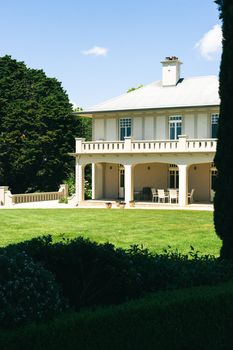 Elegant country house with lawn and patio under a clear, sunny sky.