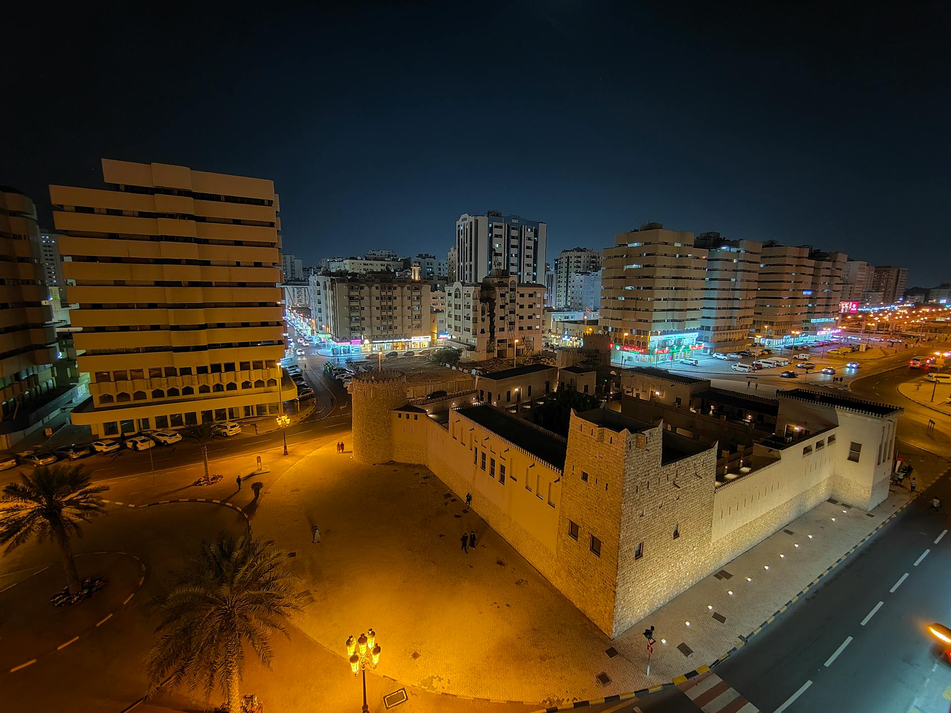 A stunning nighttime cityscape featuring a historic fort surrounded by modern buildings, lit beautifully.