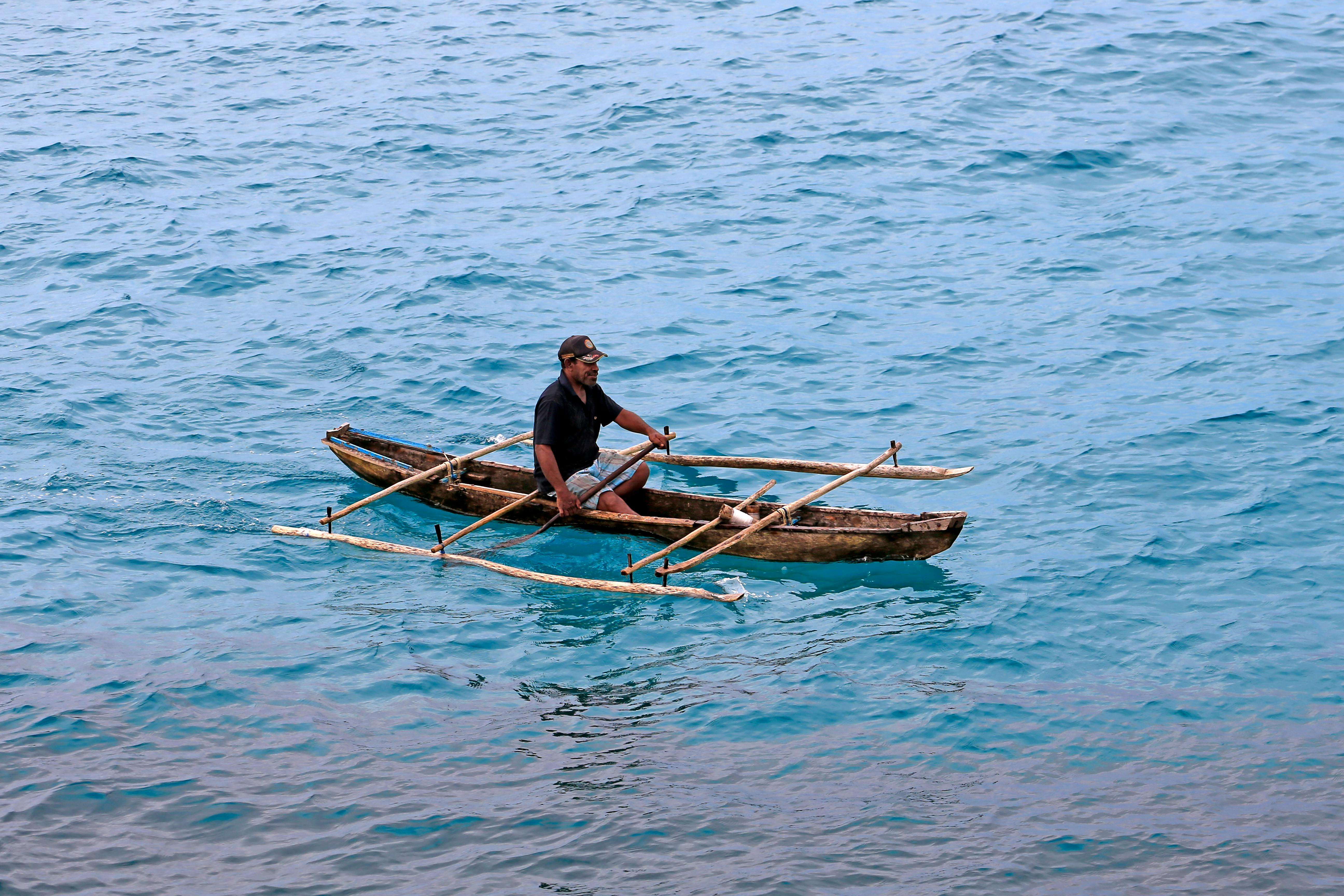 A person navigates a wooden canoe on clear blue waters, showcasing traditional seaside life.