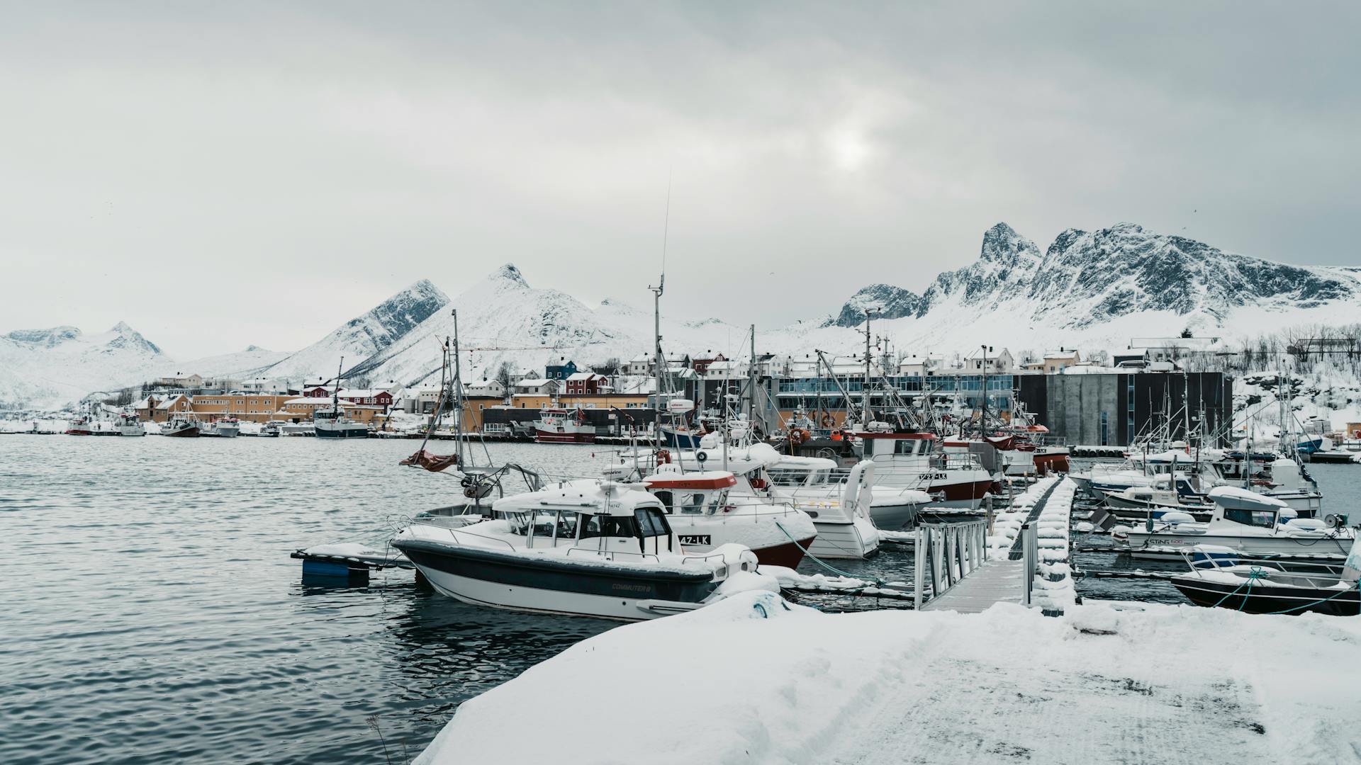 A serene snowy harbor with fishing boats docked, set against the backdrop of snow-covered mountains in Arctic Norway.