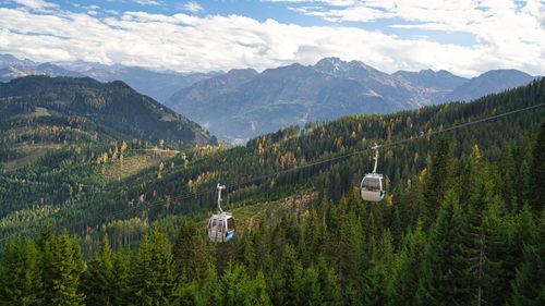 Free A cable car glides over lush forests and mountains in a beautiful alpine setting during autumn. Stock Photo