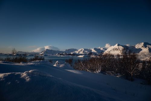 Free Peaceful winter scene with snow-covered mountains and calm lake under a clear blue sky. Stock Photo