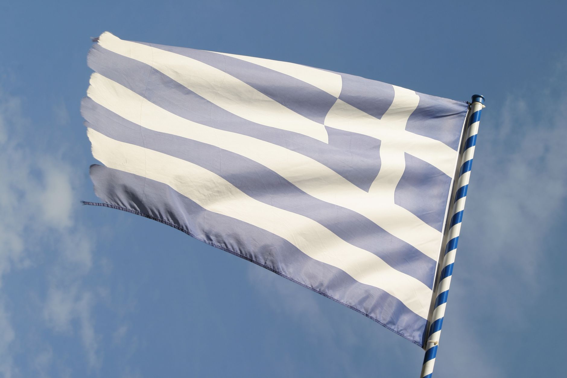 Waving Greek national flag with blue sky background, symbolizing national pride and heritage.