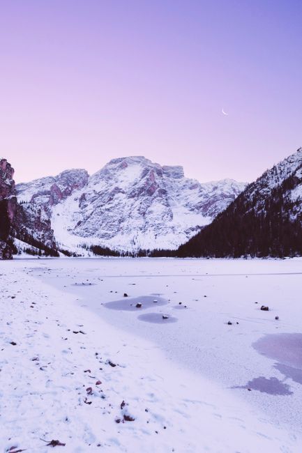 A tranquil snowy mountain landscape under a pastel sky with a crescent moon.