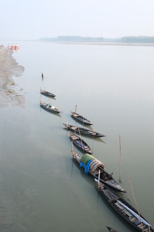Free Row of traditional wooden boats moored on a calm riverbank under a hazy sky. Stock Photo